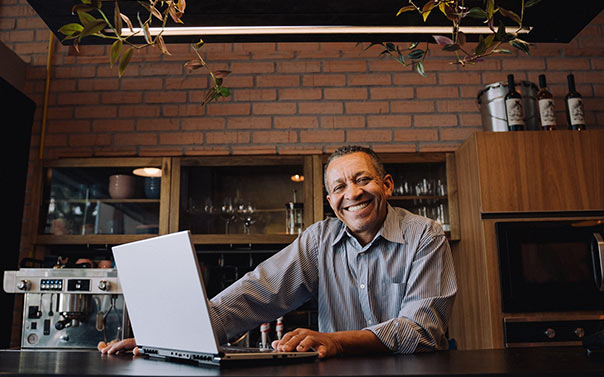 A mature male cafe owner smiling with laptop